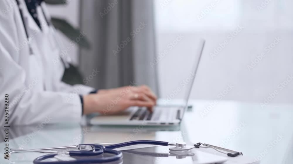 Stethoscope and medical clipboard are lying on the glass table while doctor woman is working with laptop computer on the background. Medicine and pharmacy concept Stethoscope and medical clipboard are lying on the glass table while doctor woman is working with laptop computer on the background. Medicine and pharmacy concept