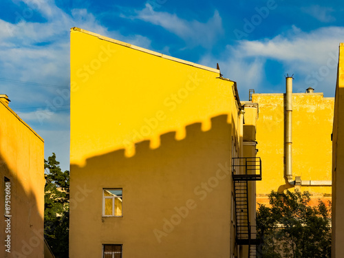 A striking image of bright yellow buildings in St. Petersburg, Russia, with shadows creating intriguing patterns on the walls. The vibrant yellow contrasts beautifully with the blue sky, creating a