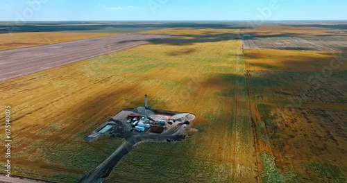 Flying closer to the site for oil production in the vast field. Several trucks surround the tower drilling the natural resources.