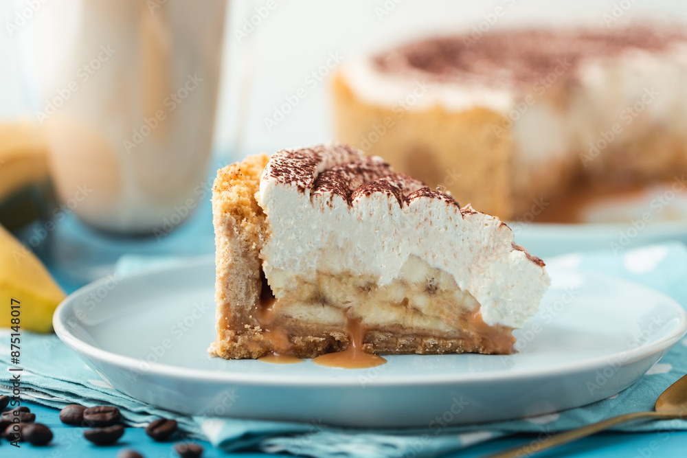 Slice of banoffe pie filled with banana and dulce de leche and sprinkled with grated chocolate. Banana cake on white plate with glass of coffee on turquoise summer background Slice of banoffe pie filled with banana and dulce de leche and sprinkled with grated chocolate. Banana cake on white plate with glass of coffee on turquoise summer background