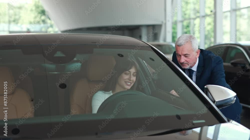 View of professional Caucasian dealer consulting his potential customer. Young girl sitting in car salon and talking with manager through open window. People discussing about advantages of auto. View of professional Caucasian dealer consulting his potential customer. Young girl sitting in car salon and talking with manager through open window. People discussing about advantages of auto.