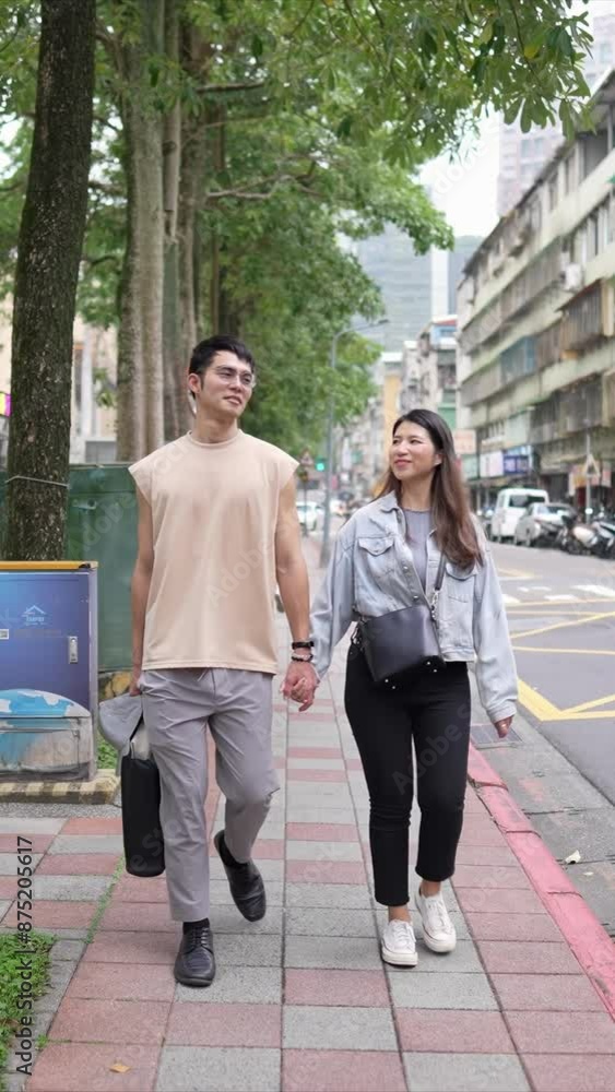 A vertical slow-motion video of a young Taiwanese couple in their twenties walking through the streets of Xinyi District, Taipei City on a spring afternoon. The man is wearing a sleeveless top A vertical slow-motion video of a young Taiwanese couple in their twenties walking through the streets of Xinyi District, Taipei City on a spring afternoon. The man is wearing a sleeveless top