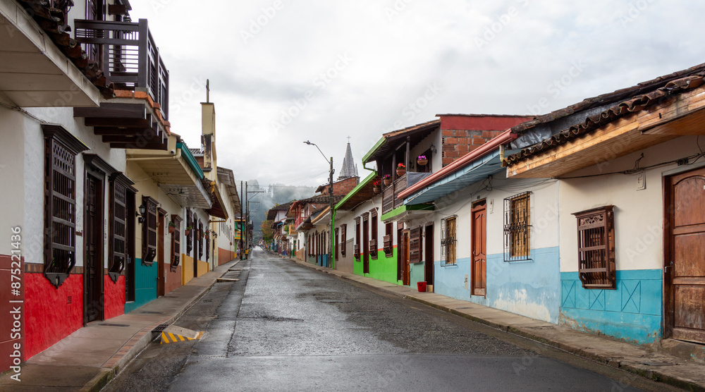 Street in Jardin, Jardín, Antioquia, Colombia. Green background, colorful colonial facades and houses. Clouds, church in the background. Street in Jardin, Jardín, Antioquia, Colombia. Green background, colorful colonial facades and houses. Clouds, church in the background.