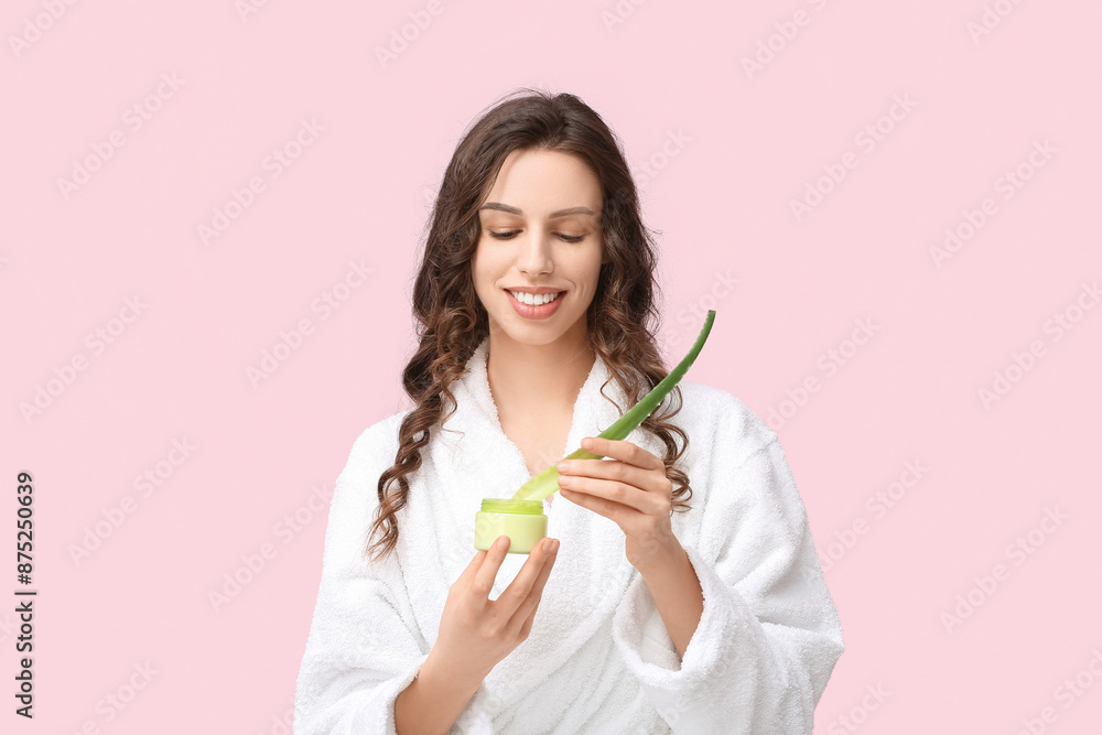 Beautiful young woman in bathrobe with aloe vera and jar of cream against color background Beautiful young woman in bathrobe with aloe vera and jar of cream against color background