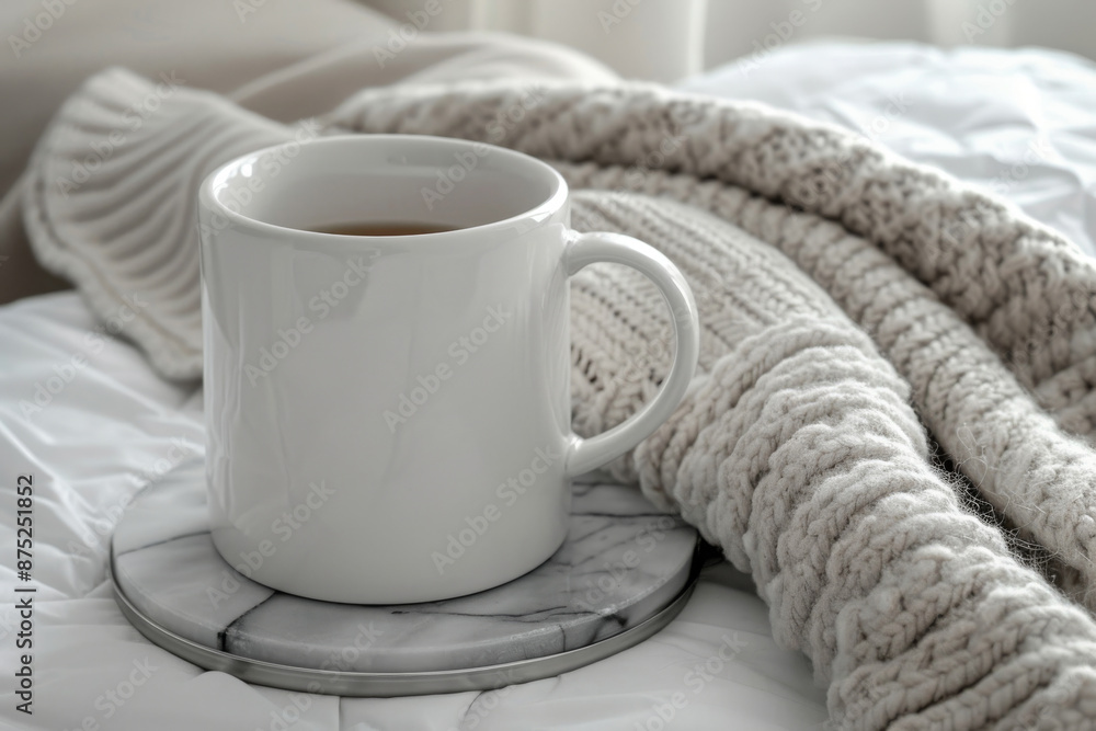 White coffee mug placed on an elegant marble coaster, beside a soft fabric texture of a grey knitted blanket. White coffee mug placed on an elegant marble coaster, beside a soft fabric texture of a grey knitted blanket.