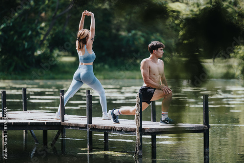 Young couple stretching and exercising on a wooden bridge in nature by a serene lake. Embracing outdoor fitness and healthy lifestyle in a natural setting.
