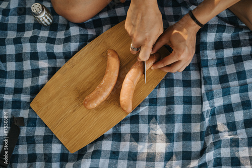 Foto Close-up of friends hands cutting sausages on a wooden board during a picnic outdoors on a blue checkered blanket