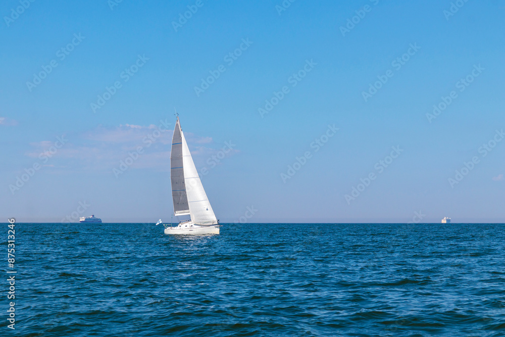 Obraz premium White sloop rigged yacht sailing in the Baltic sea at sunset. Clear sky after the storm, soft sunlight. Transportation, travel, cruise, sport, recreation, leisure activity, racing, regatta