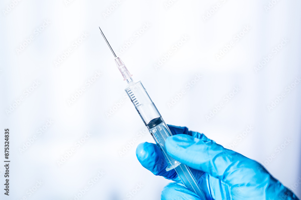 Human hand wearing medical gloves holds a syringe needle,Doctor hands with syringe on light background Human hand wearing medical gloves holds a syringe needle,Doctor hands with syringe on light background