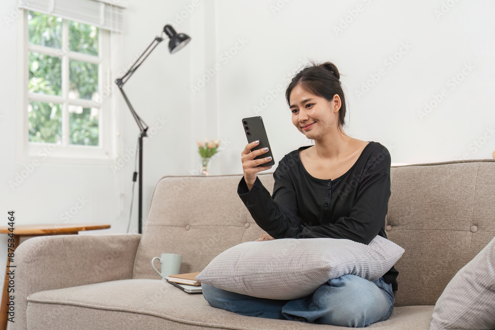 Woman Using Smartphone to Follow Online News While Relaxing on Sofa at Home in Modern Living Room Woman Using Smartphone to Follow Online News While Relaxing on Sofa at Home in Modern Living Room
