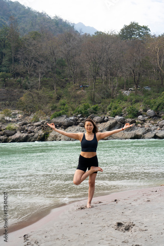 India, Rishikesh, March 27, 2024. Asian beautiful young woman does yoga near Ganges.