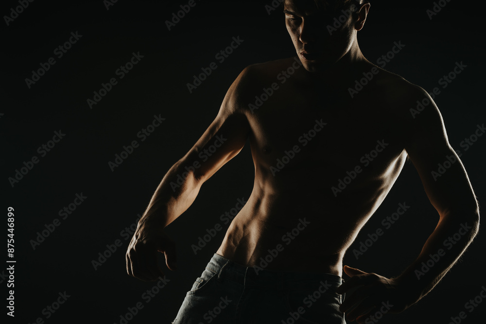 Silhouette of a muscular shirtless man posing against a dark background showcasing strength and fitness Silhouette of a muscular shirtless man posing against a dark background showcasing strength and fitness