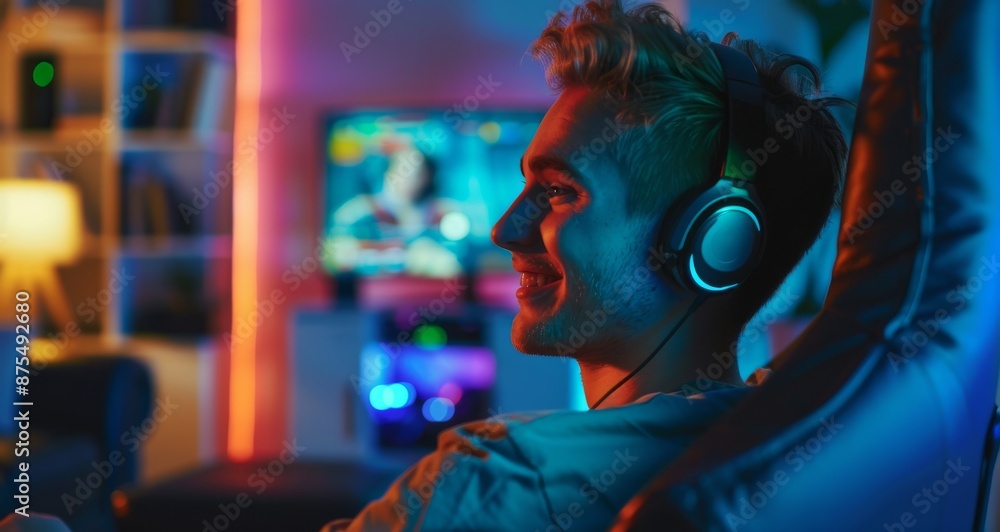 Obraz premium Smiling gamer in headphones enjoying online gaming session in neon-lit room