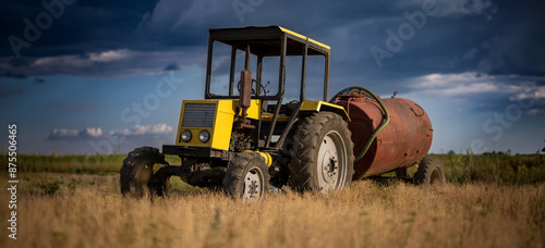 Old yellow tractor in the field with a barrel photo