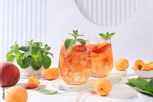 Ice peach tea or cocktail with mint and apricots, a recipe for a refreshing summer drink. Two glasses with peach fruit lemonade on a light table, detox diet and weight loss concept, 