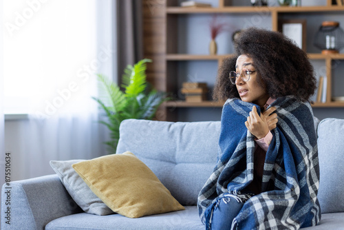 Cuadro en lienzo Woman sitting on a sofa wrapped in a warm blanket, visibly feeling cold