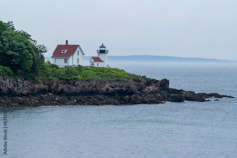 White lighthouse with smaller houses on rocky point near ocean and bay