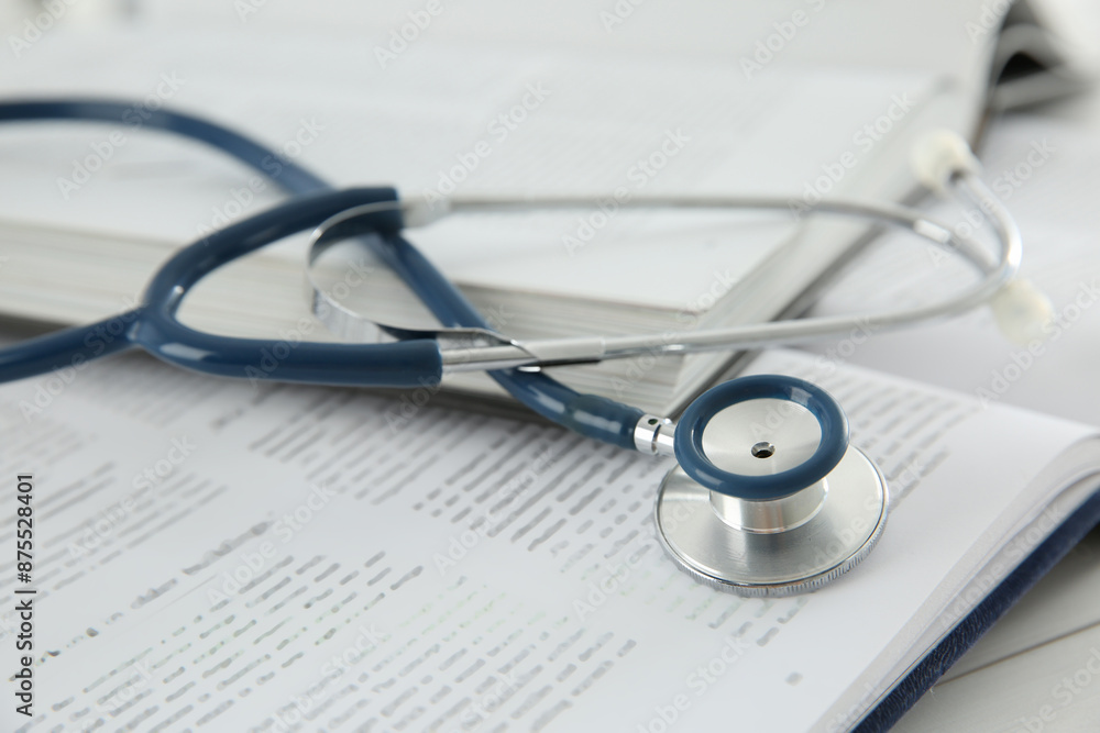 One new medical stethoscope and books on white wooden table, closeup One new medical stethoscope and books on white wooden table, closeup