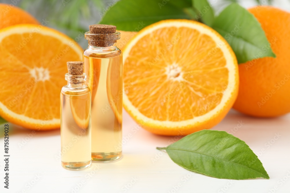 Essential oils in bottles, oranges and green leaves on white table Essential oils in bottles, oranges and green leaves on white table