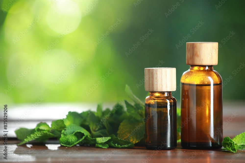 Bottles of mint essential oil and fresh leaves on wooden table, space for text Bottles of mint essential oil and fresh leaves on wooden table, space for text