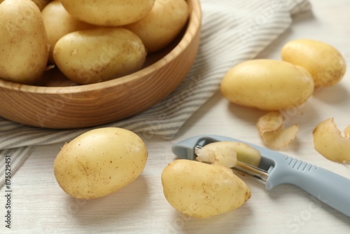 Canvas Print Fresh raw potatoes, peels and peeler on white wooden table