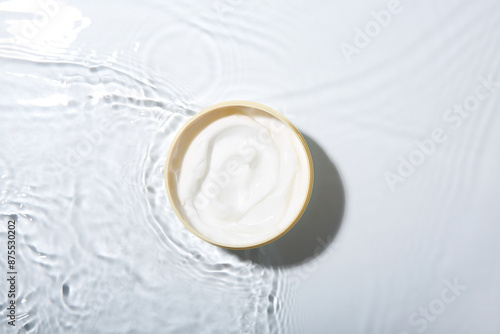 Cosmetic product. Jar with cream in water on light background, top view