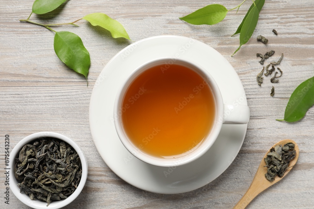 Refreshing green tea in cup, spoon and leaves on light wooden table, flat lay Refreshing green tea in cup, spoon and leaves on light wooden table, flat lay