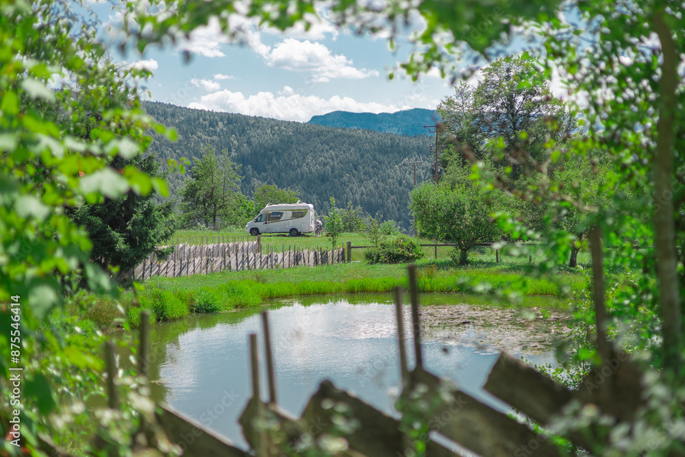 Small campervan or RV parked in beautiful picturesque surrounding in front of a lake and before beautiful mountain backdrop. Epic view of camper van in nature