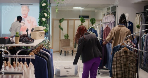 African american clients in fashion boutique donating their clothes for good cause. Customers placing garments in donation box, doing philanthropy gesture in clothing store photo