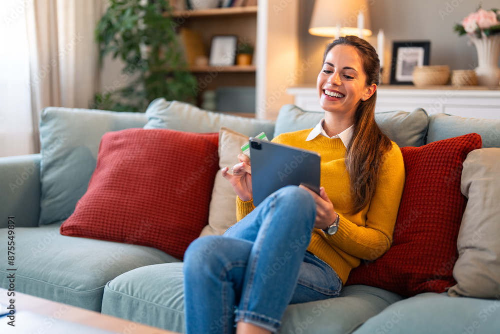 Happy woman on the couch shopping online at home in the living room. Happy young woman shopping online through digital tablet using credit card at home. Happy woman on the couch shopping online at home in the living room. Happy young woman shopping online through digital tablet using credit card at home.