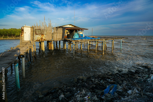 A peaceful sunset view of a wooden house stretching into the sea, with waves gently lapping the sandy shore