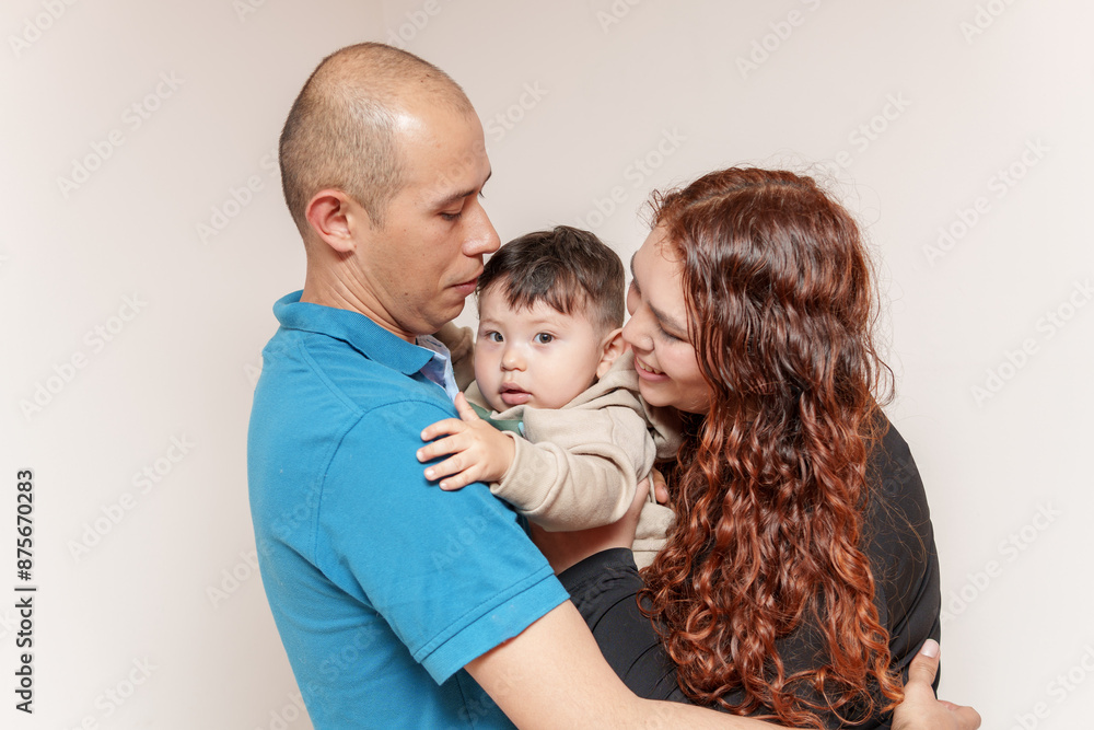 A man and a woman are holding a baby. The baby is smiling and the man is wearing a blue shirt. The woman has red hair and is wearing a black shirt. Scene is happy and loving A man and a woman are holding a baby. The baby is smiling and the man is wearing a blue shirt. The woman has red hair and is wearing a black shirt. Scene is happy and loving