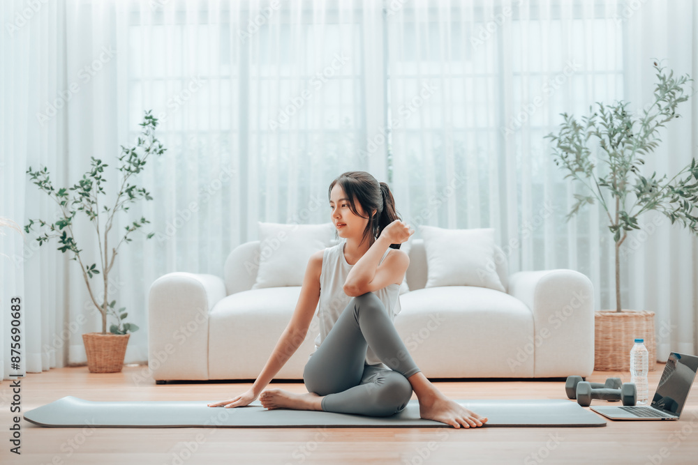 Young Asian woman stretching yoga workout on exercise mat while online training class with computer laptop in living room Young Asian woman stretching yoga workout on exercise mat while online training class with computer laptop in living room