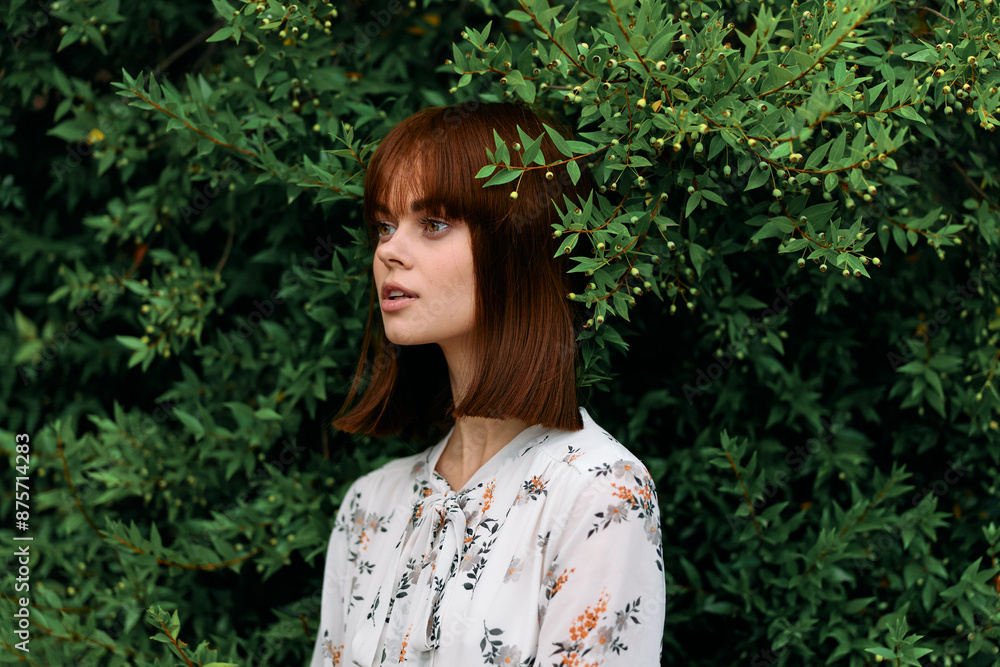 Vibrant redhead woman standing gracefully in front of lush green leafed bush Vibrant redhead woman standing gracefully in front of lush green leafed bush