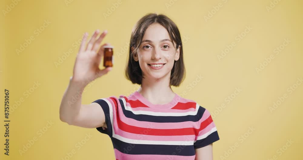 Young woman smiling and showing a small brown pill bottle in a bright setting Young woman smiling and showing a small brown pill bottle in a bright setting