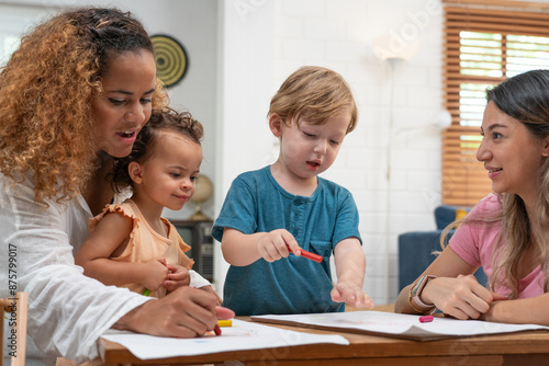 Happy family. Mother and kids together paint. Woman helps the child. Little children with kindergarten teacher drawing at table indoors. Learning and playing	