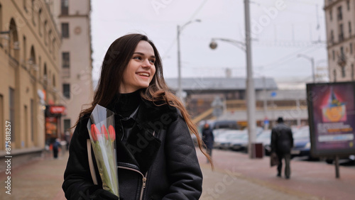 Portrait of a happy brunette girl with a tulip in the background of the city in the cold season.