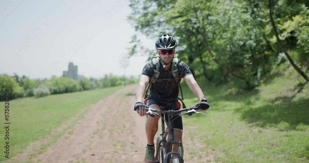 Man riding a mountainbike on a dusty path with scenic countryside background. Front view portrait. Dirtroad next to a green meadow. Man riding a mountainbike on a dusty path with scenic countryside background. Front view portrait. Dirtroad next to a green meadow.