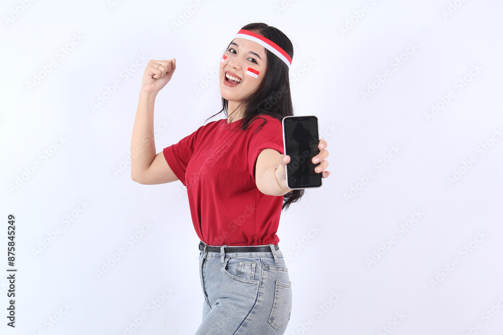 Excited young Asian woman clenched fist with red white flag ribbon showing mobile phone with blank screen for advertising, celebrating victory Indonesian independence day 17 Agustus Excited young Asian woman clenched fist with red white flag ribbon showing mobile phone with blank screen for advertising, celebrating victory Indonesian independence day 17 Agustus