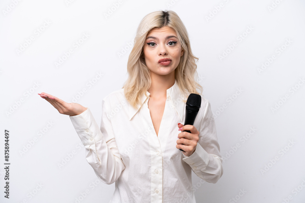 Young singer woman picking up a microphone isolated on white background having doubts while raising hands Young singer woman picking up a microphone isolated on white background having doubts while raising hands