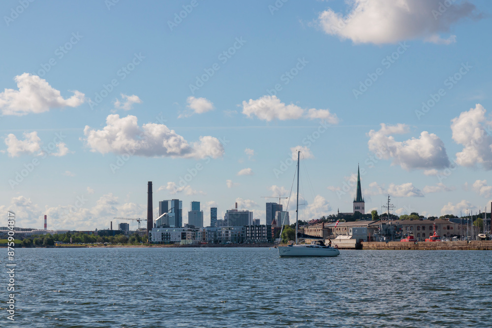 Naklejka premium Tallinn silhouette and a sailboat from distance - sea side. Baltic sea Tallinn in front. Clear summer weather - July in Estonia.