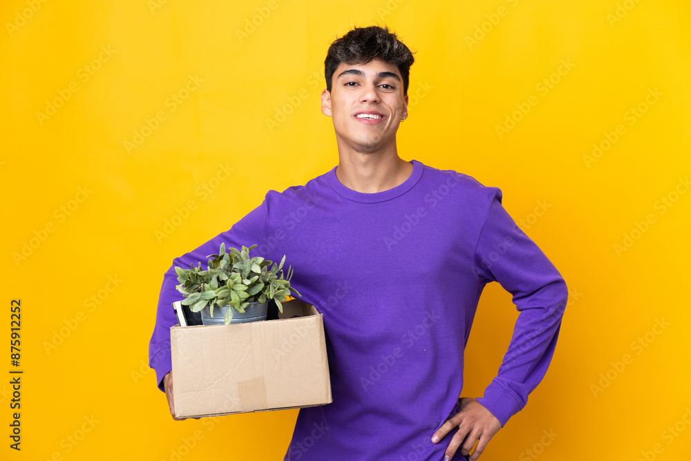 Man making a move while picking up a box full of things posing with arms at hip and smiling Man making a move while picking up a box full of things posing with arms at hip and smiling