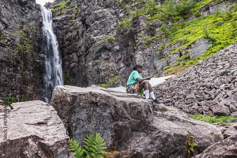 Woman sits and takes a rest with her mobile phone at Sweden's highest waterfall Njupeskär. Woman sits and takes a rest with her mobile phone at Sweden's highest waterfall Njupeskär.