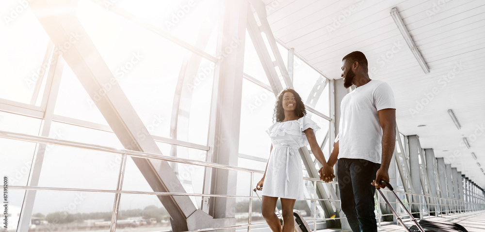 A happy couple walks hand-in-hand through a bright airport terminal, pulling luggage behind them. The man is wearing a white t-shirt and jeans, while the woman is wearing a white dress. A happy couple walks hand-in-hand through a bright airport terminal, pulling luggage behind them. The man is wearing a white t-shirt and jeans, while the woman is wearing a white dress.