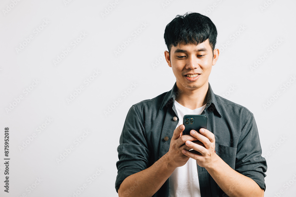 An enthusiastic Asian teenager smiles while typing a text message on his smart mobile phone for online communication. Studio shot isolated on white background, highlighting his enjoyment of technology An enthusiastic Asian teenager smiles while typing a text message on his smart mobile phone for online communication. Studio shot isolated on white background, highlighting his enjoyment of technology