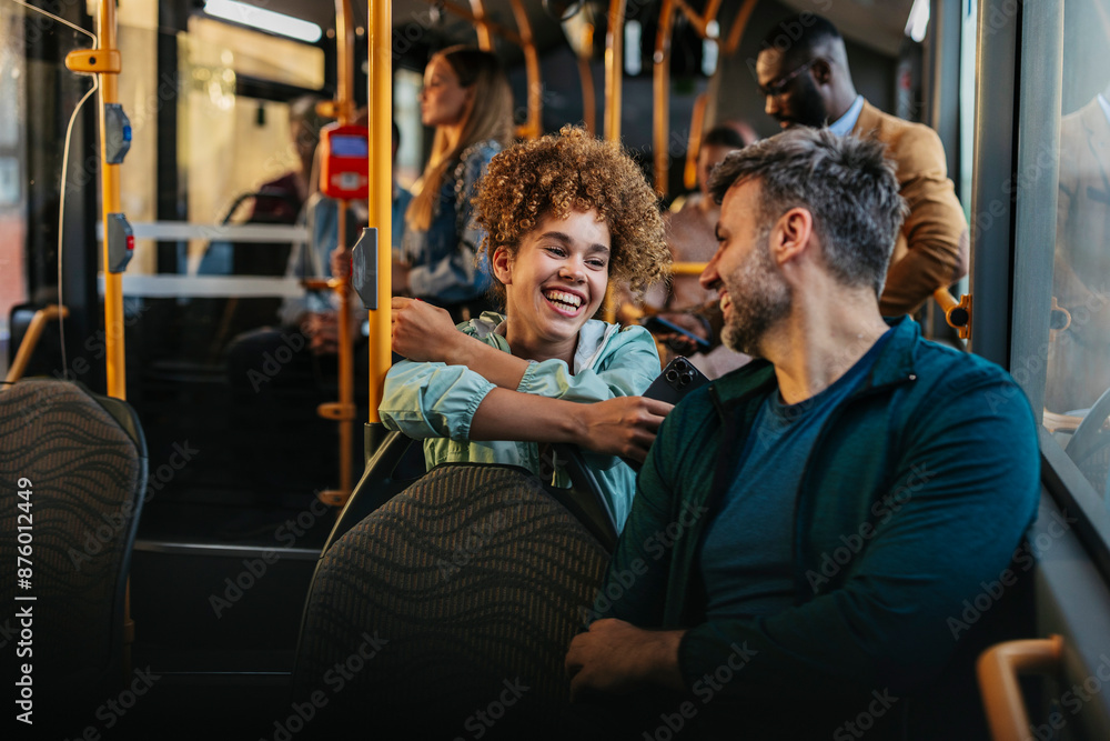 Fototapeta premium Friends laughing and talking in a crowded bus, she with smart phone