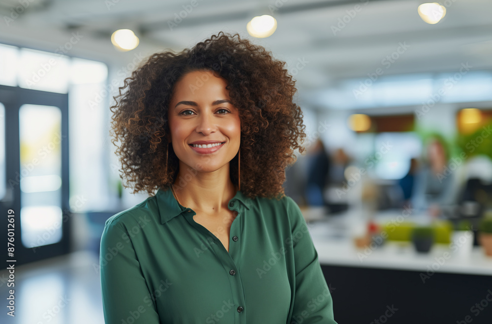 Smiling businesswoman with curly hair, wearing a green shirt, standing confidently in a modern office setting Smiling businesswoman with curly hair, wearing a green shirt, standing confidently in a modern office setting