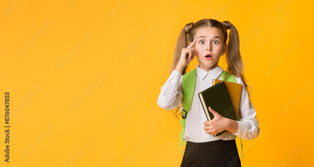 Oops. Elementary Student Girl Looking At Camera Holding Books On Yellow Background, Empty Space Oops. Elementary Student Girl Looking At Camera Holding Books On Yellow Background, Empty Space