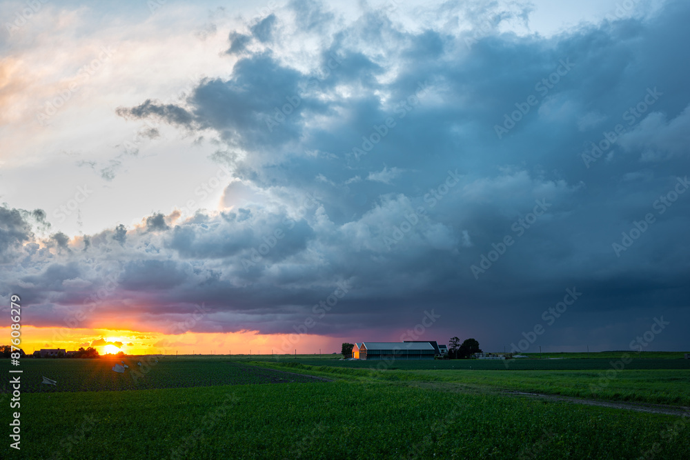 Beautiful summer landscape of a thunderstorm over the Dutch countryside at sundown. A farm is illuminated by the last light of the setting sun. Beautiful summer landscape of a thunderstorm over the Dutch countryside at sundown. A farm is illuminated by the last light of the setting sun.