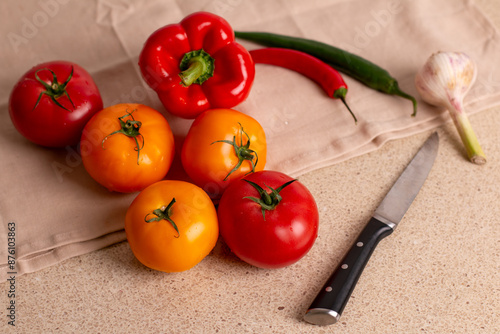 Fresh wet red and yellow tomatoes with peppers, garlic and a knife on a table